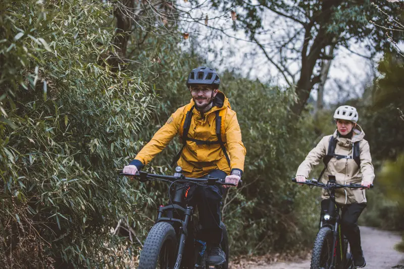 Two riders on fat-tyre e-bikes on a dirt trail through the bush