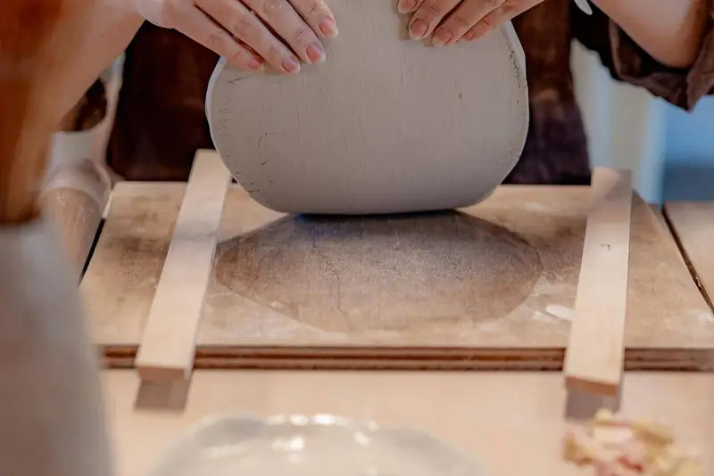 Hands lifting a rolled slab of clay at the workbench