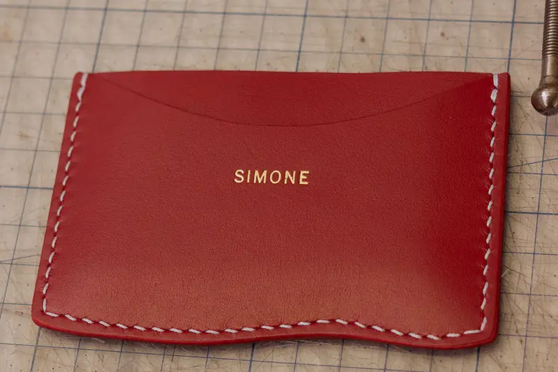 A finished red card wallet, saddle-stitched and stamped with a name